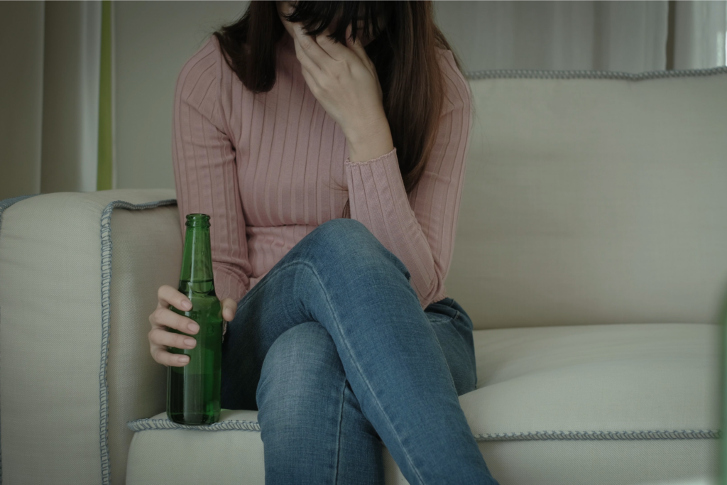 woman sitting on the couch holding a bottle of beer showing signs that someone is an alcoholic